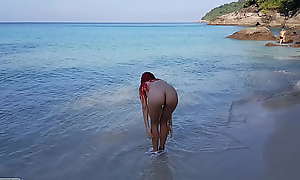 Naked red-haired girl bathes on a public beach